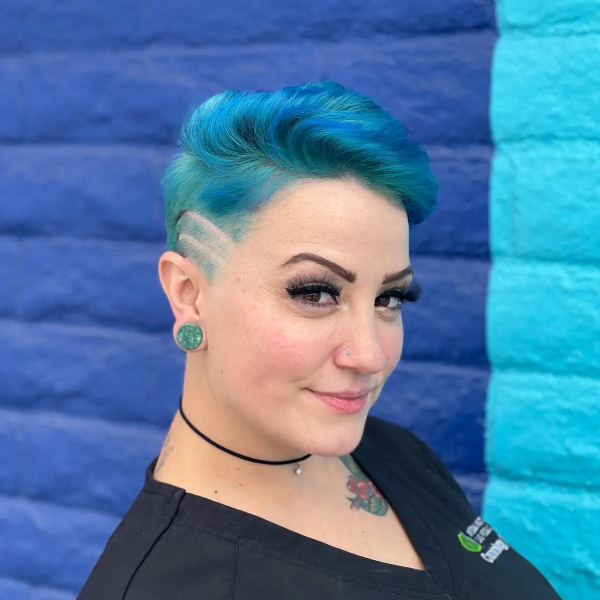 Vivid blue short haircut with curved shaved-line design against a teal and blue wall by Cuts By Soc
